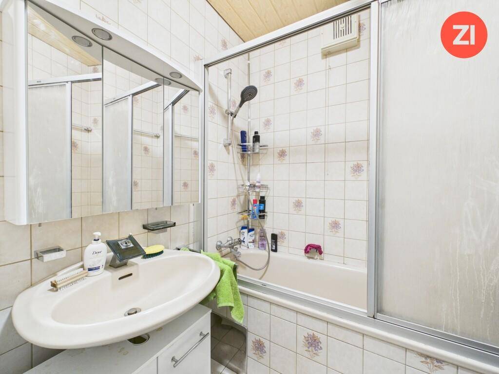 Badezimmer mit Badewanne, Duschabtrennung und gemusterten Wandfliesen.