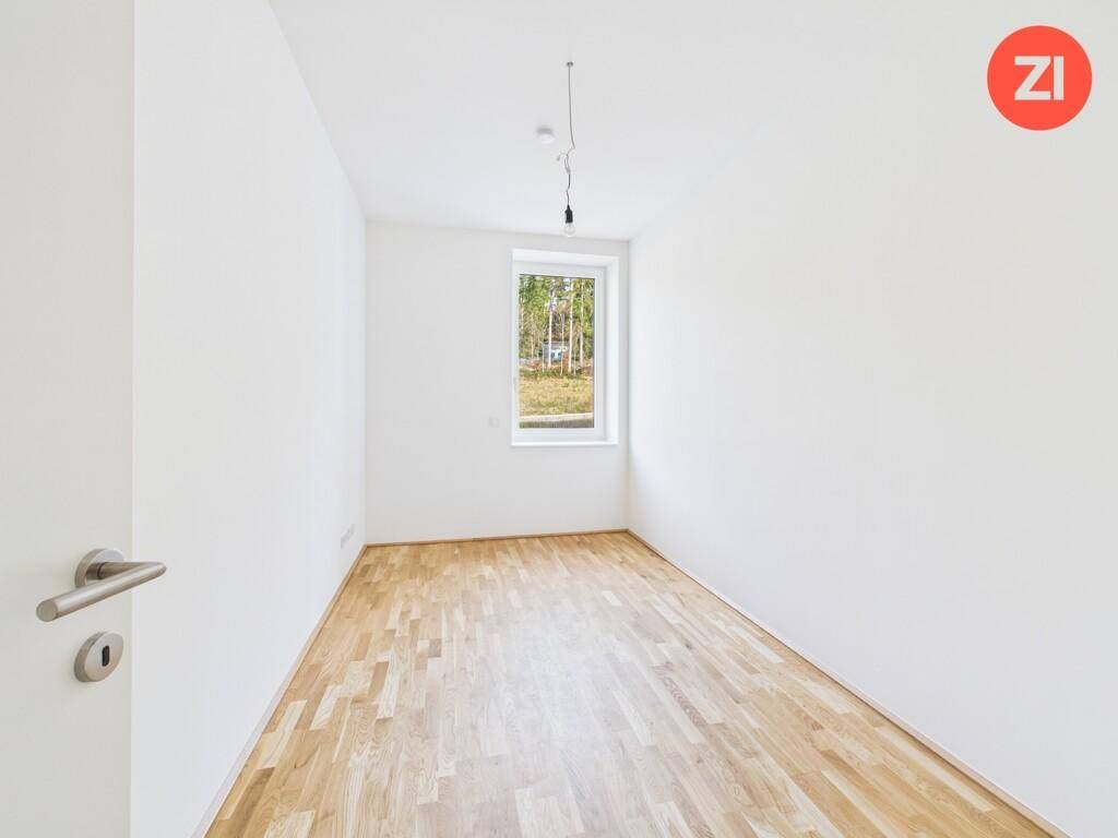 Helles Schlafzimmer mit Parkettboden und einem Fenster mit Blick ins Grüne.