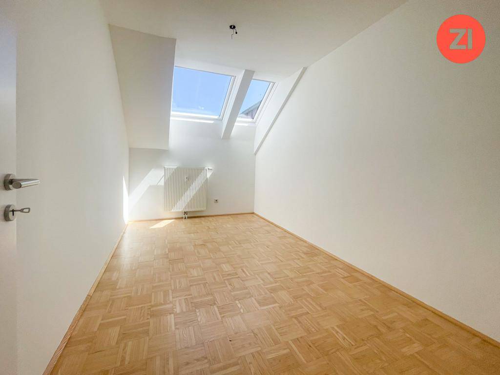 Helles Zimmer mit Parkettboden, Dachschrägen und einem großen Dachfenster für viel Tageslicht.