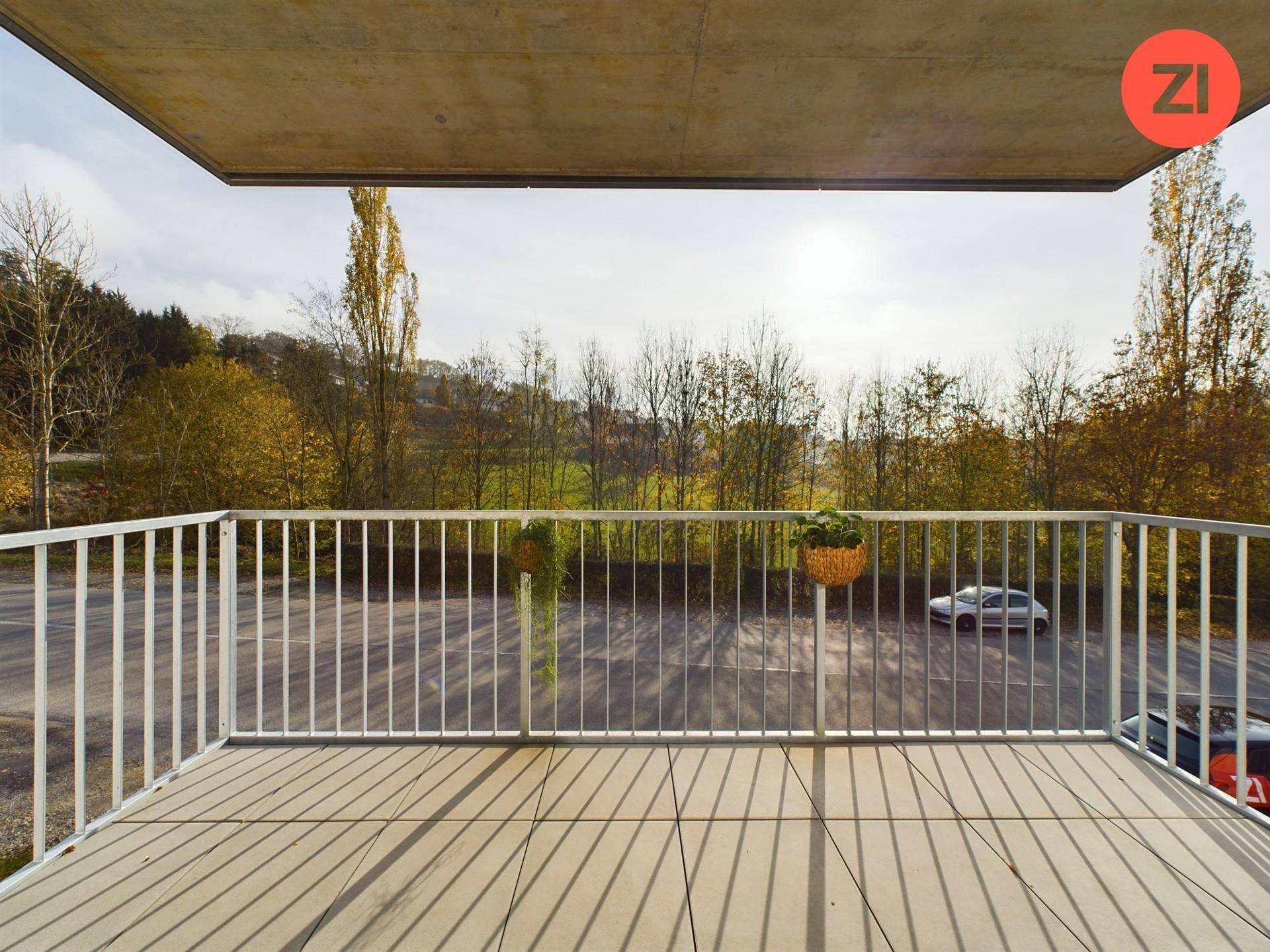 Geräumiger Balkon mit Fliesenboden und weitem Blick auf die umliegende Natur und Parkplätze.