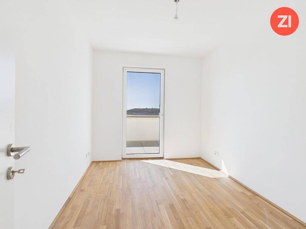 Helles Zimmer mit Holzboden und einer Tür, die zu einem französischen Balkon oder einer kleinen Terrasse führt.