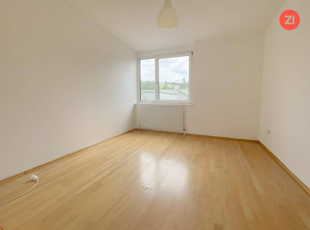 Leeres Zimmer mit hellem Holzfußboden und einem Fenster, das viel Tageslicht hereinlässt.