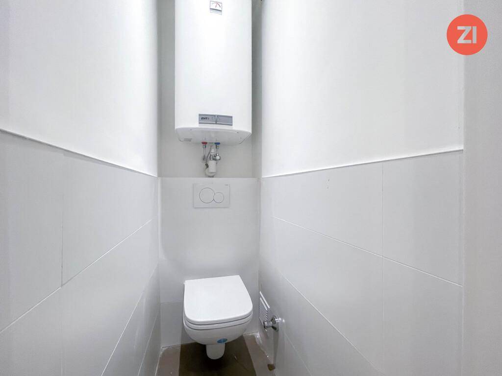 Separates WC mit wandhängender Toilette und Boiler, komplett gefliest in Weiß.