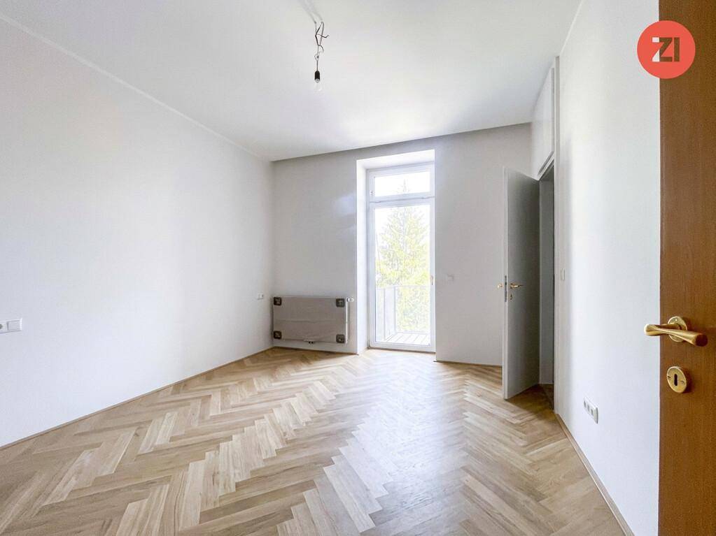 Heller Raum mit Fischgrätparkett und Zugang zu einem Balkon, ideal für entspannte Stunden im Freien.