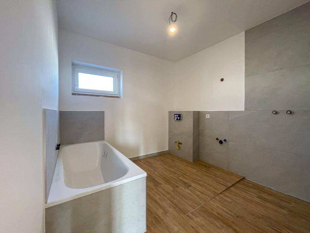 Modernes Badezimmer im Rohbau mit Badewanne und Fenster.