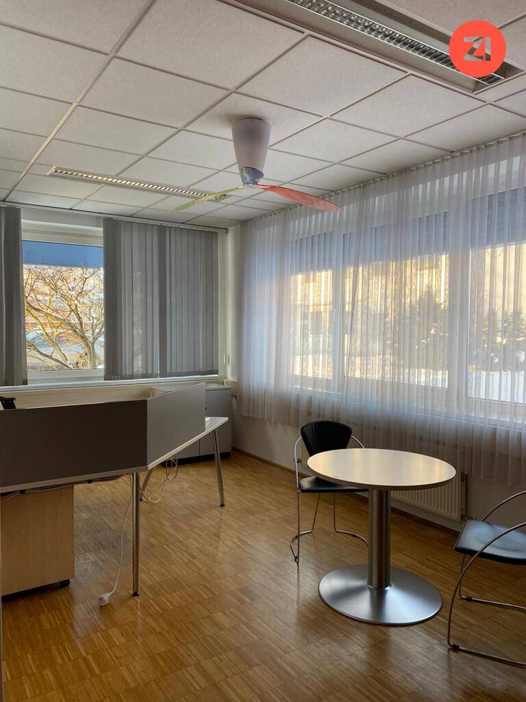 Heller Büroraum mit Holzboden, Fensterfront und Jalousien, funktional eingerichtet.