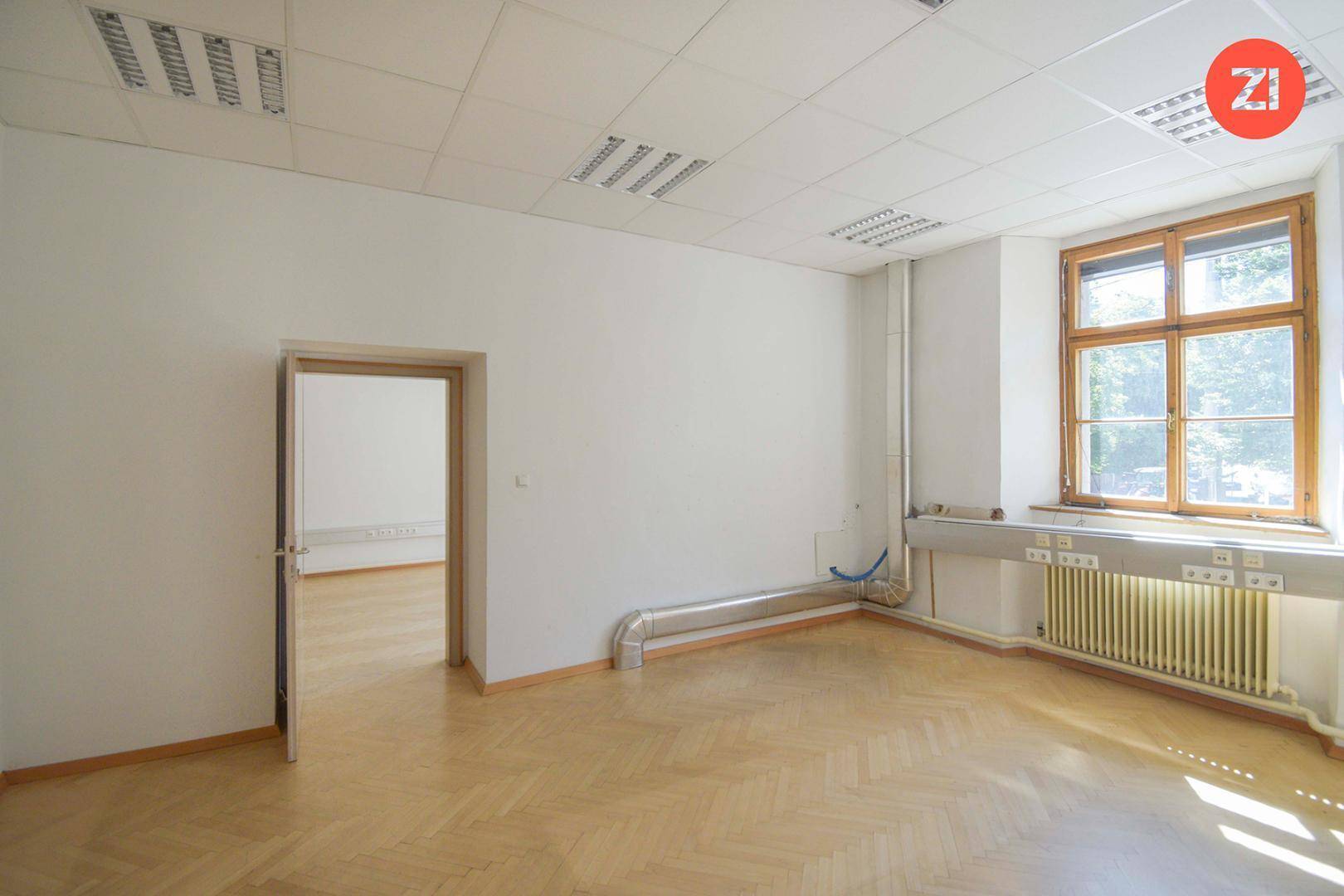 Helles Büro mit Fischgrätparkett, großem Fenster und sichtbaren Rohren, bietet einen funktionalen Raum.