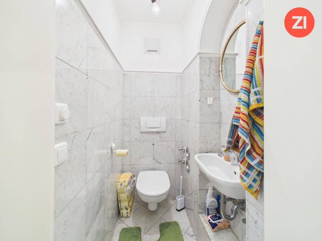 Kleines Gäste-WC mit Marmorfliesen, Toilette und einem runden Spiegel über dem Waschbecken.