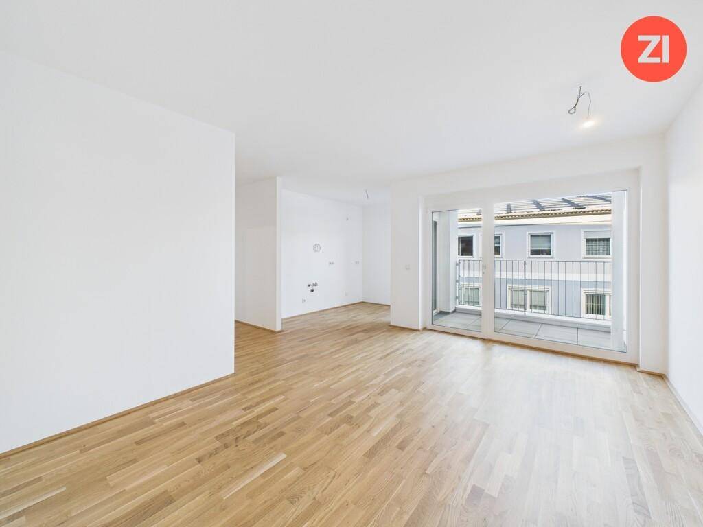 Heller, leerer Wohnbereich mit Parkettboden und Zugang zu einem Balkon.