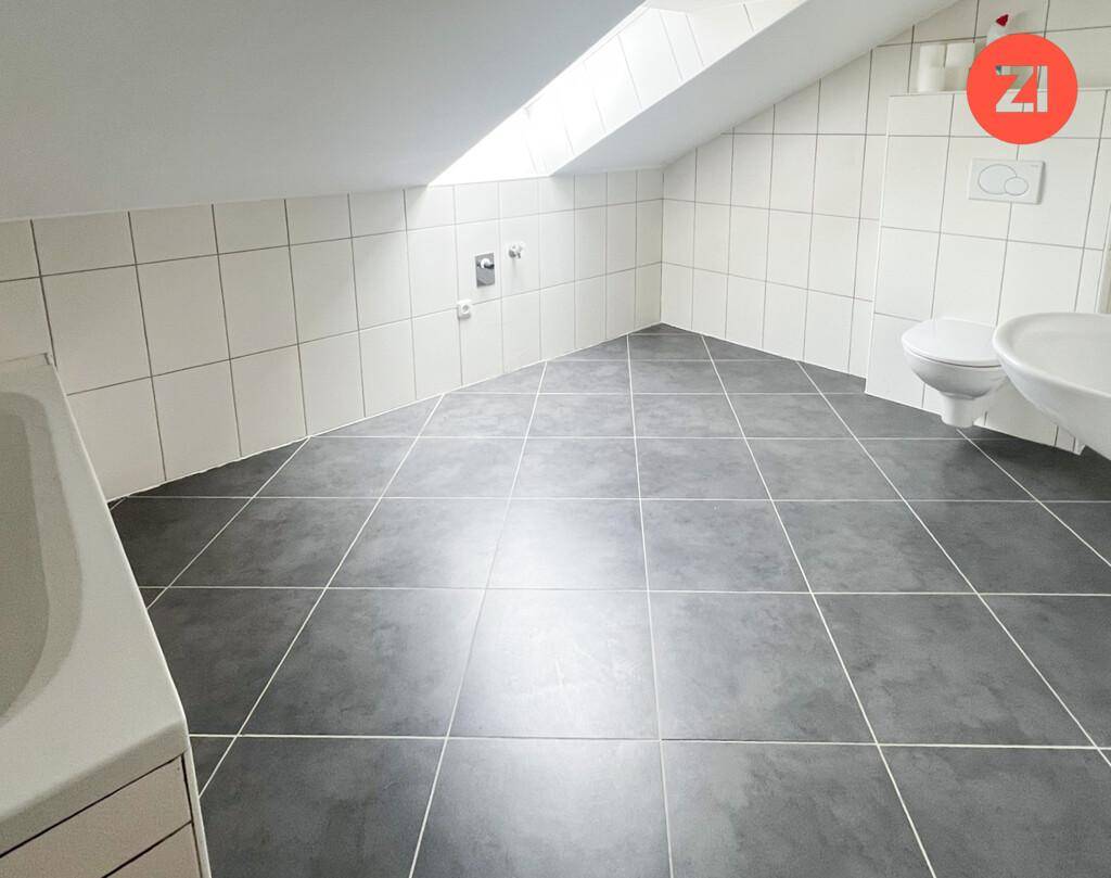 Gefliestes Badezimmer im Dachgeschoss mit Badewanne, Toilette und Dachfenster für Tageslicht.
