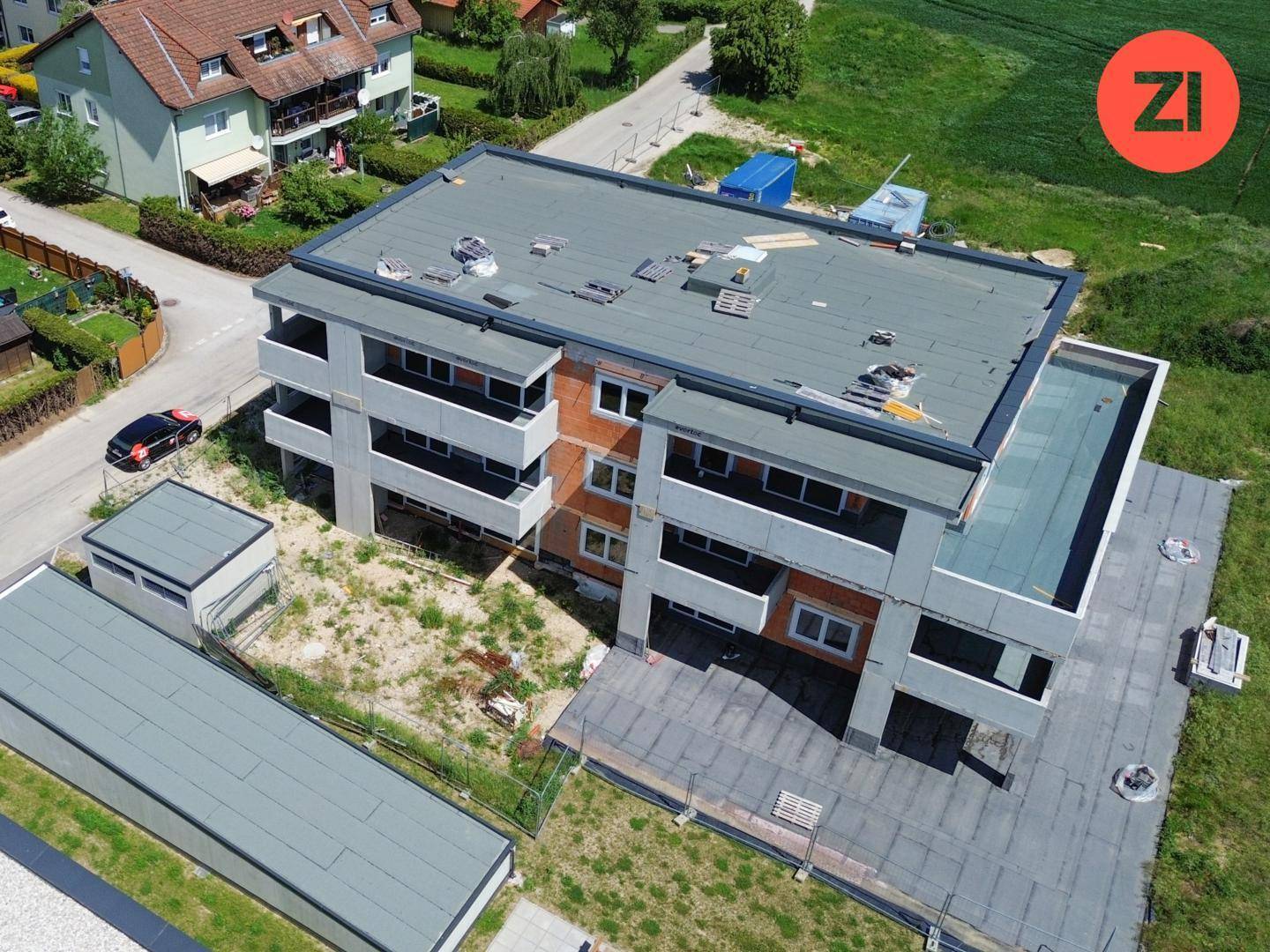 Luftaufnahme eines im Bau befindlichen Mehrfamilienhauses mit Flachdach und Balkonen in ländlicher Lage.