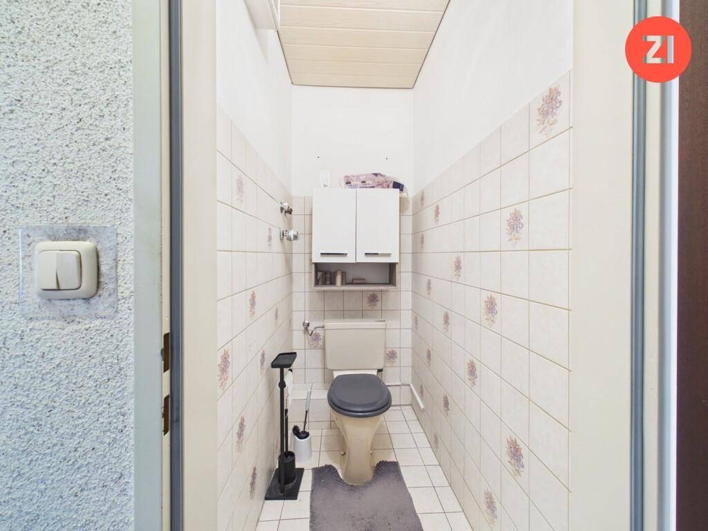 Kleines WC mit Toilette, Waschbecken und weißen Fliesen.