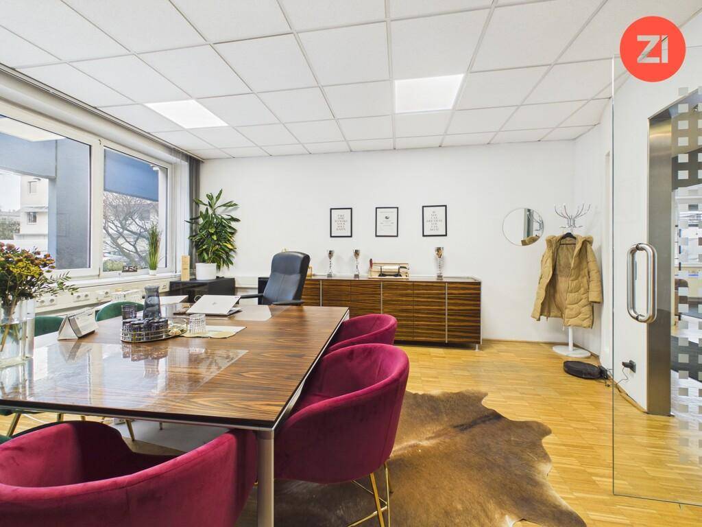 Helles Büro mit Holzboden, modernem Holztisch, roten Stühlen und einem Sideboard an der Wand.
