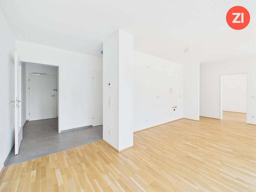 Offener Wohnbereich mit hellem Holzboden und Übergang zu einem gefliesten Eingangsbereich.
