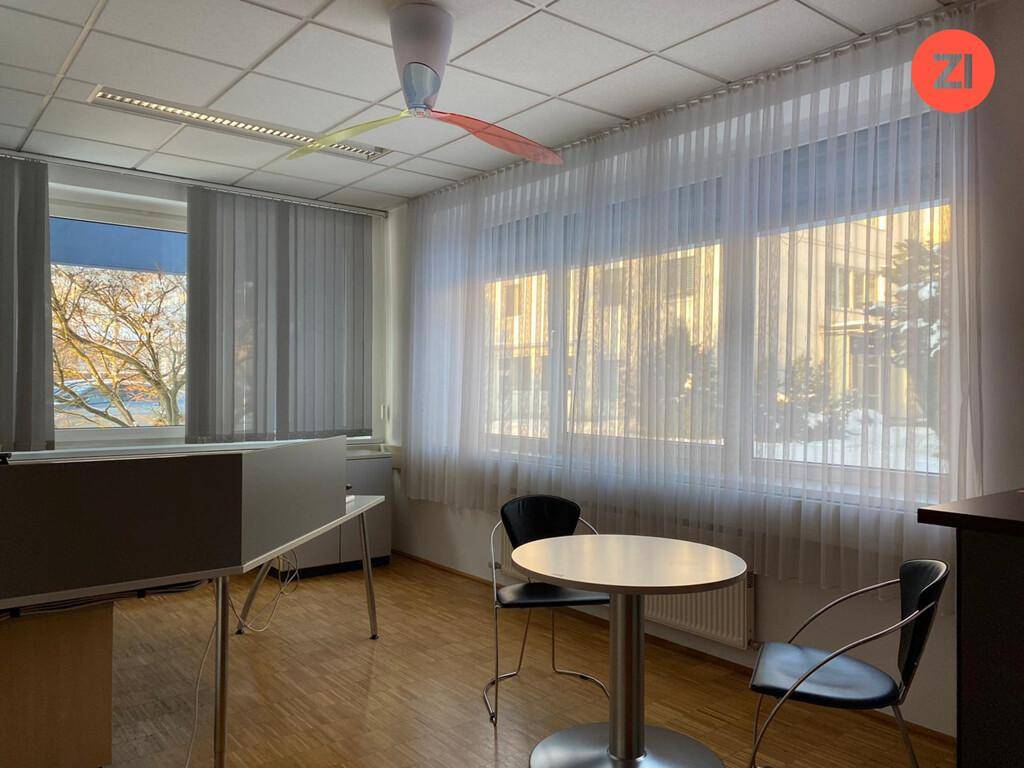 Heller Büroraum mit Holzboden, Fensterfront und Jalousien, funktional eingerichtet.