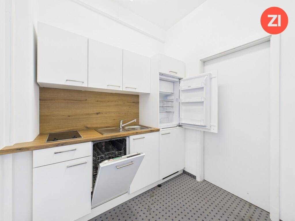 Kompakte Küchenzeile mit weißen Schränken, Holz-Arbeitsplatte und integrierten Geräten wie Geschirrspüler und Kühlschrank.