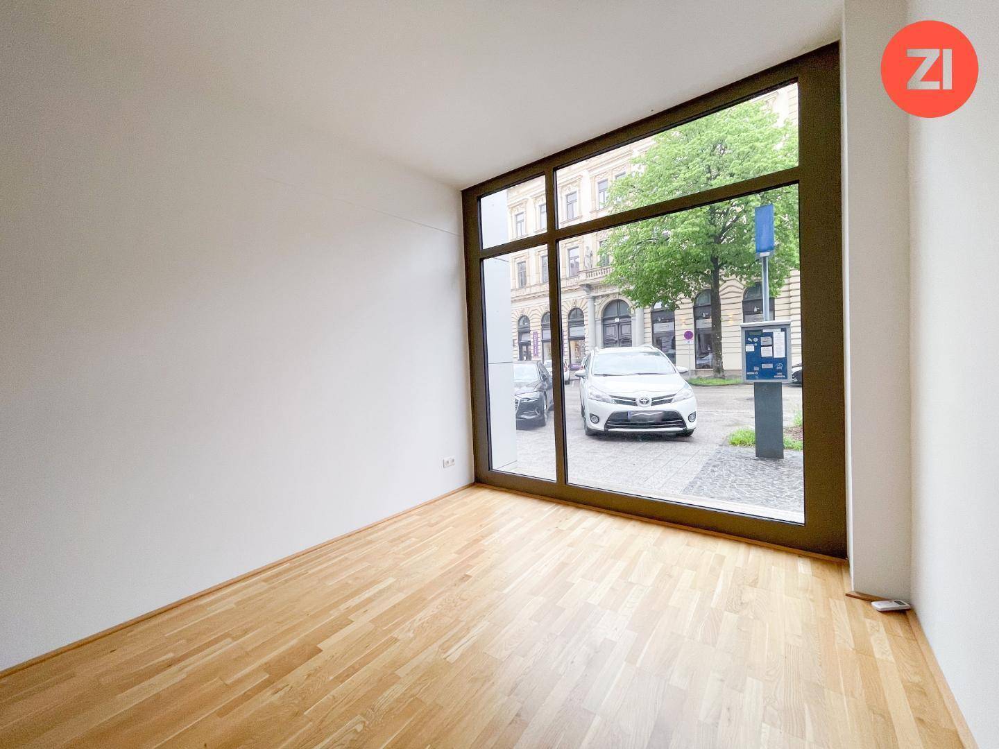 Kleiner, heller Büroraum mit Holzboden und einem großen Fenster, das viel Tageslicht hereinlässt.