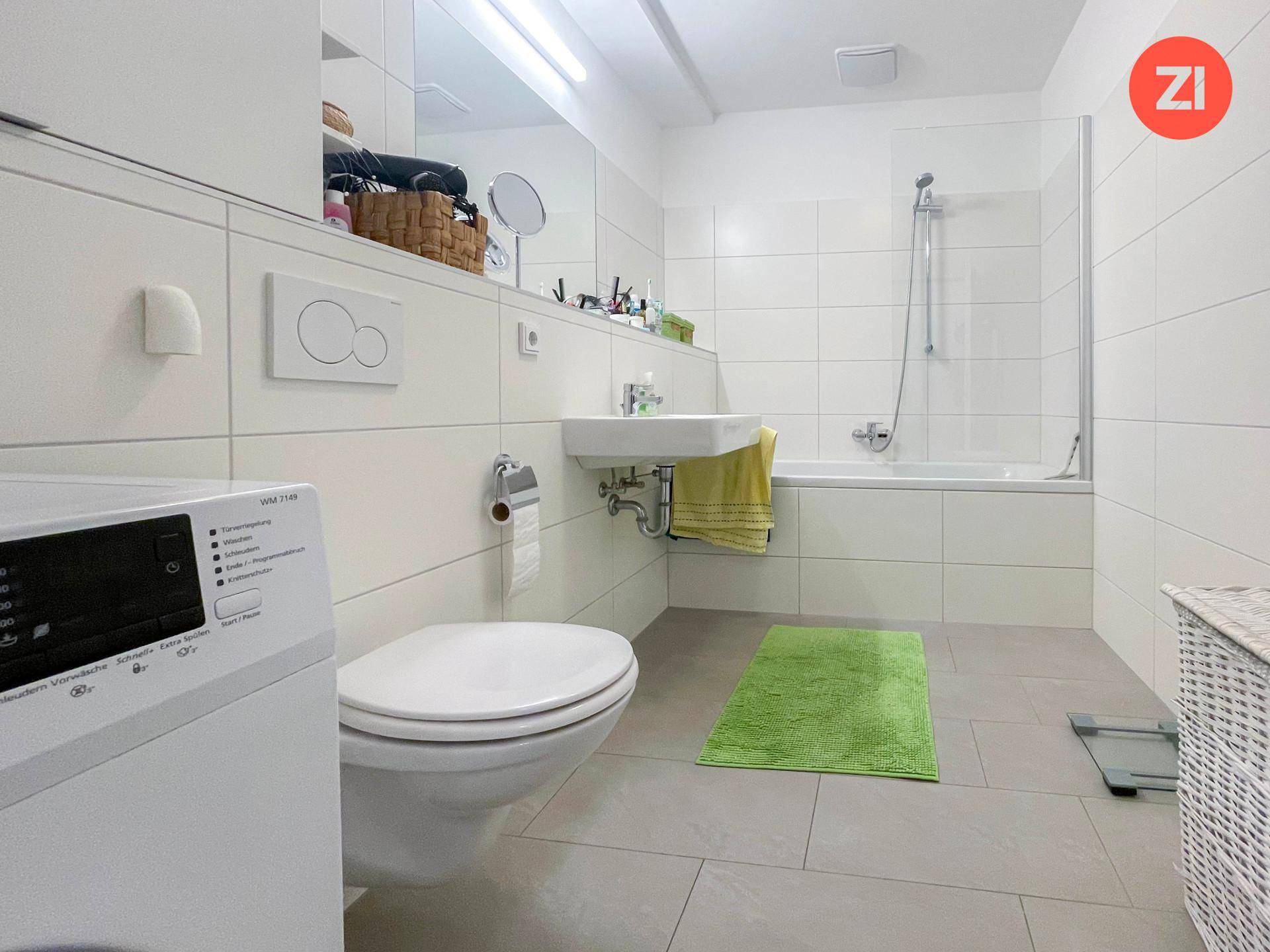 Helles Badezimmer mit Badewanne, Dusche, WC und Waschmaschine, modern gefliest.