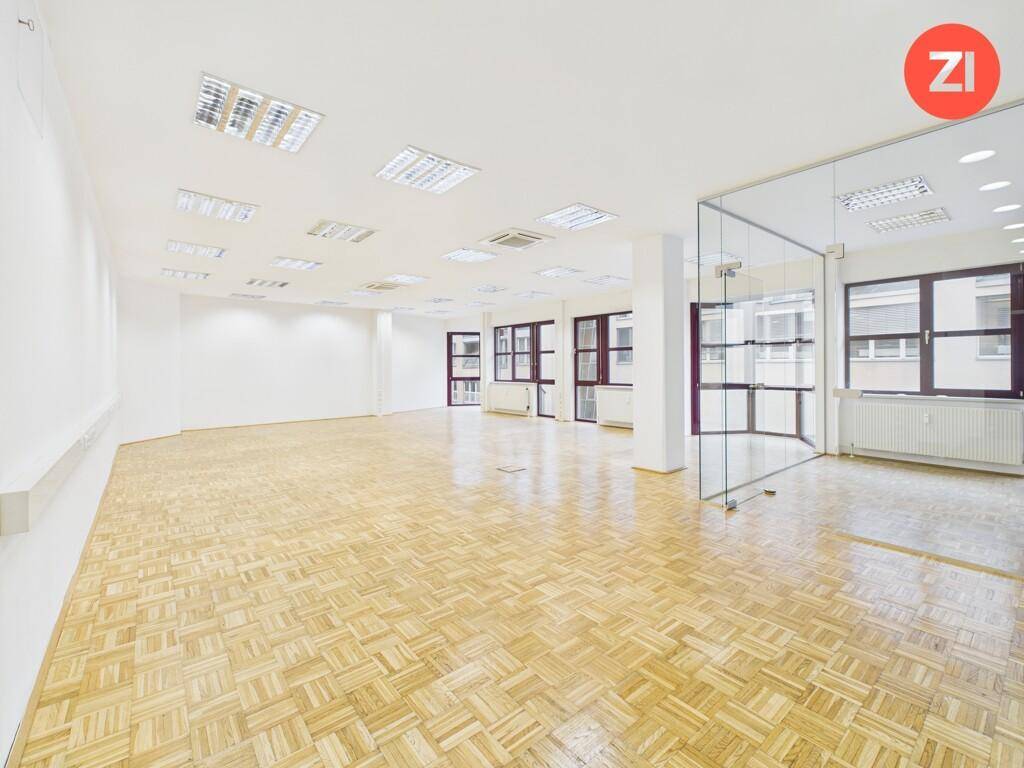 Geräumiges, leeres Büro mit hellem Parkettboden, weißen Wänden und modernen Glasabtrennungen, ideal für flexible Arbeitsbereiche.