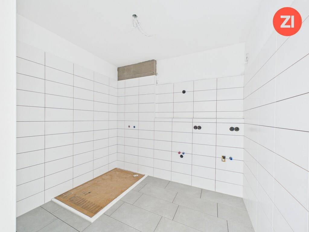 Unfertiges Badezimmer mit weißen Wandfliesen und vorbereitetem Bereich für eine Dusche.