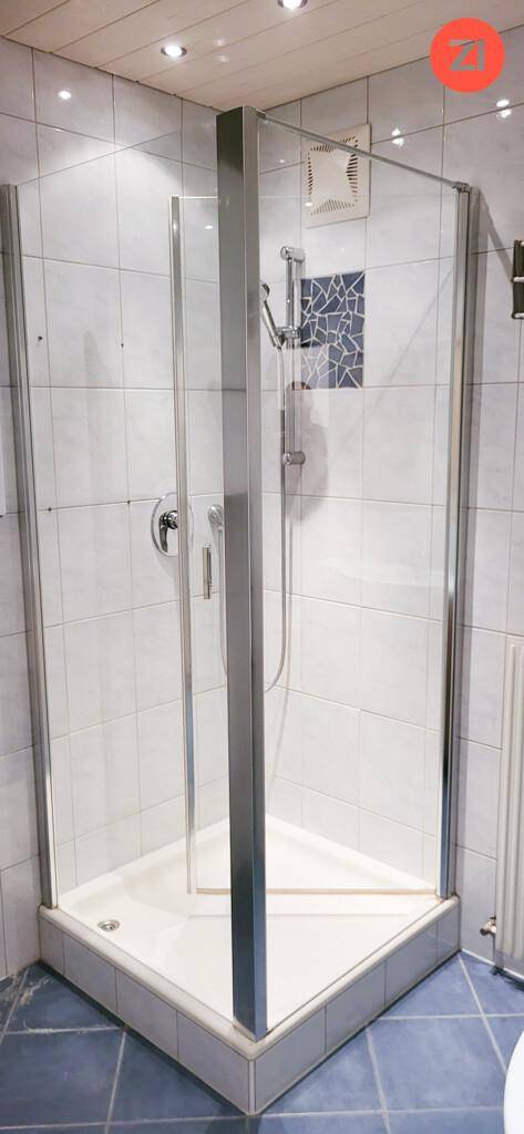 Eckdusche mit Glaswänden und weißem Fliesenboden in einem gepflegten Badezimmer.