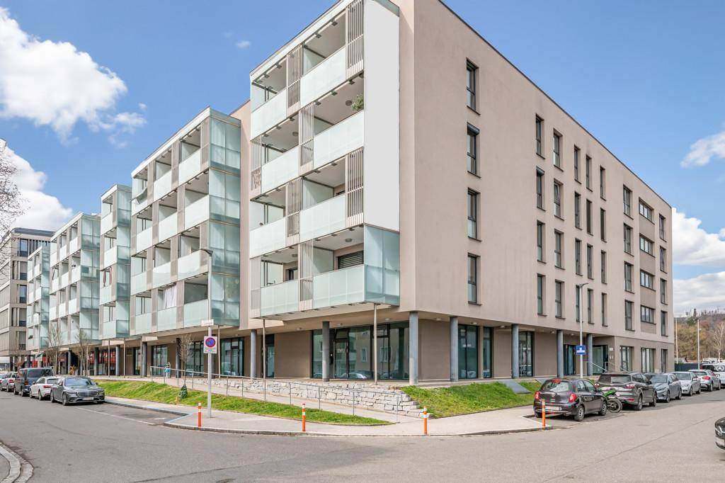 Moderne Wohnanlage an einer Straßenecke mit Geschäften im Erdgeschoss und vielen Balkonen.