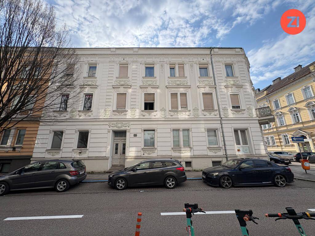 Detailansicht der weißen Fassade eines Altbaus mit dekorativen Elementen und Fenstern.