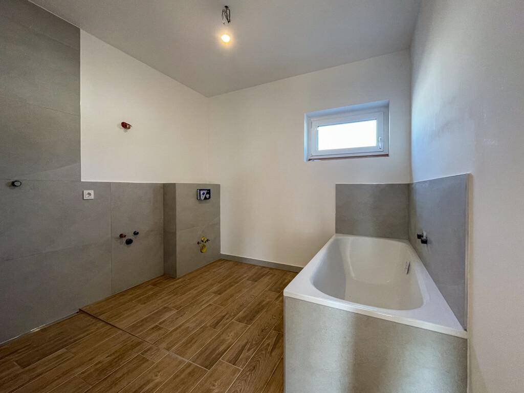 Modernes Badezimmer im Bau mit Badewanne, Holzoptikfliesen und Fenster, bereit für die Endmontage.