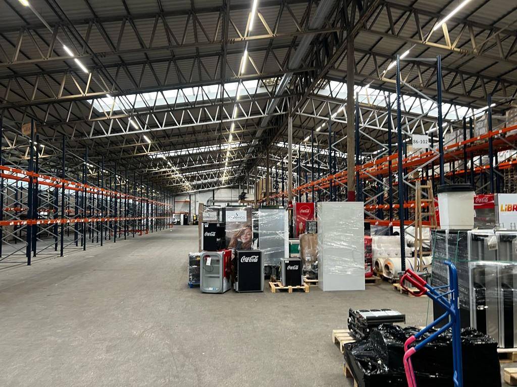 Innenansicht einer großen Lagerhalle mit hohen Decken, Palettenregalen und verschiedenen Waren auf Paletten.