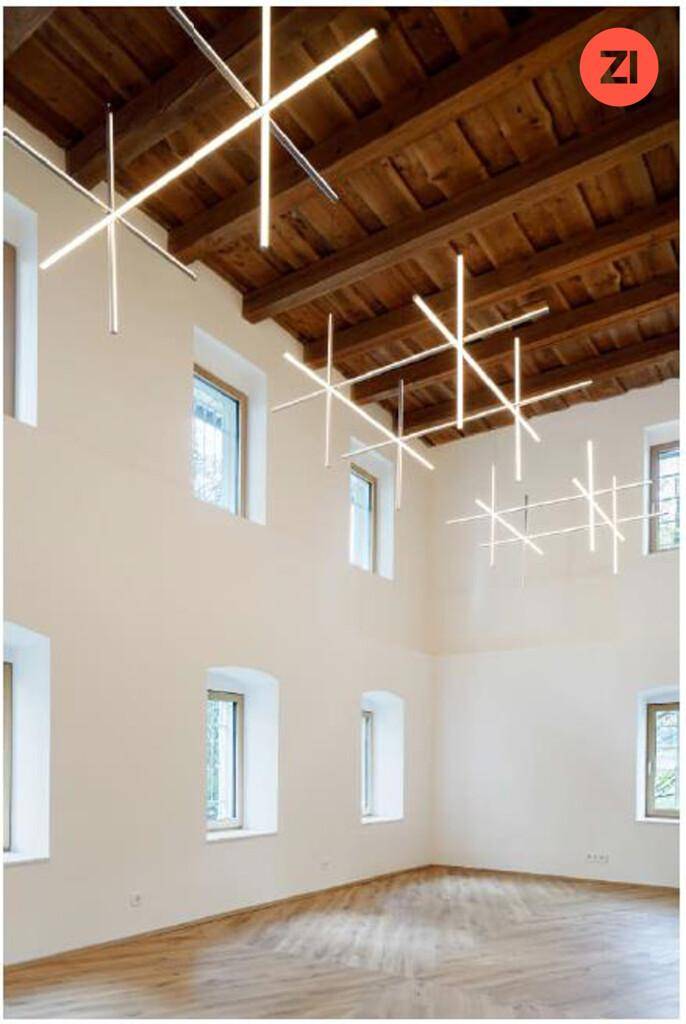 Hoher Raum mit sichtbaren Holzbalken an der Decke und modernen linearen Beleuchtungselementen.