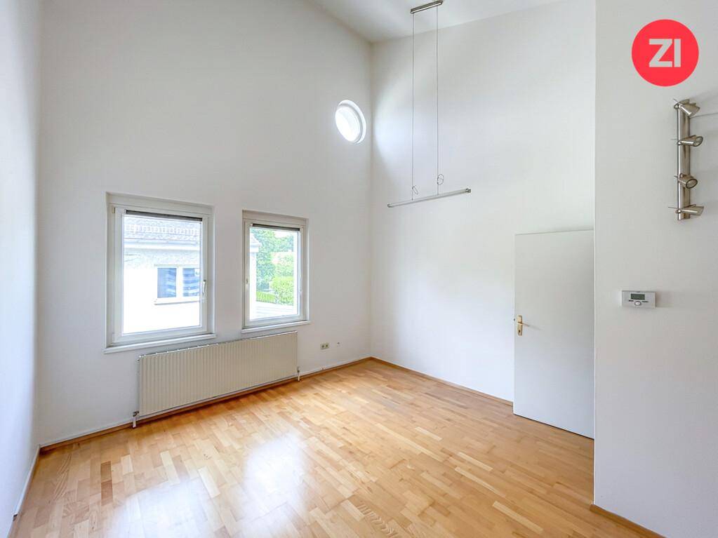 Geräumiger Raum mit hohen Decken, Holzfußboden und zwei Fenstern für viel Tageslicht.