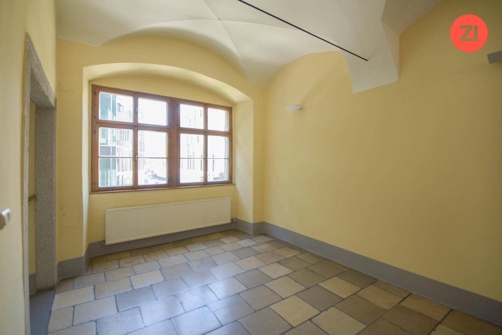 Raum mit gelben Wänden, Fliesenboden und großem Fenster mit Heizkörper, vielseitig nutzbar.
