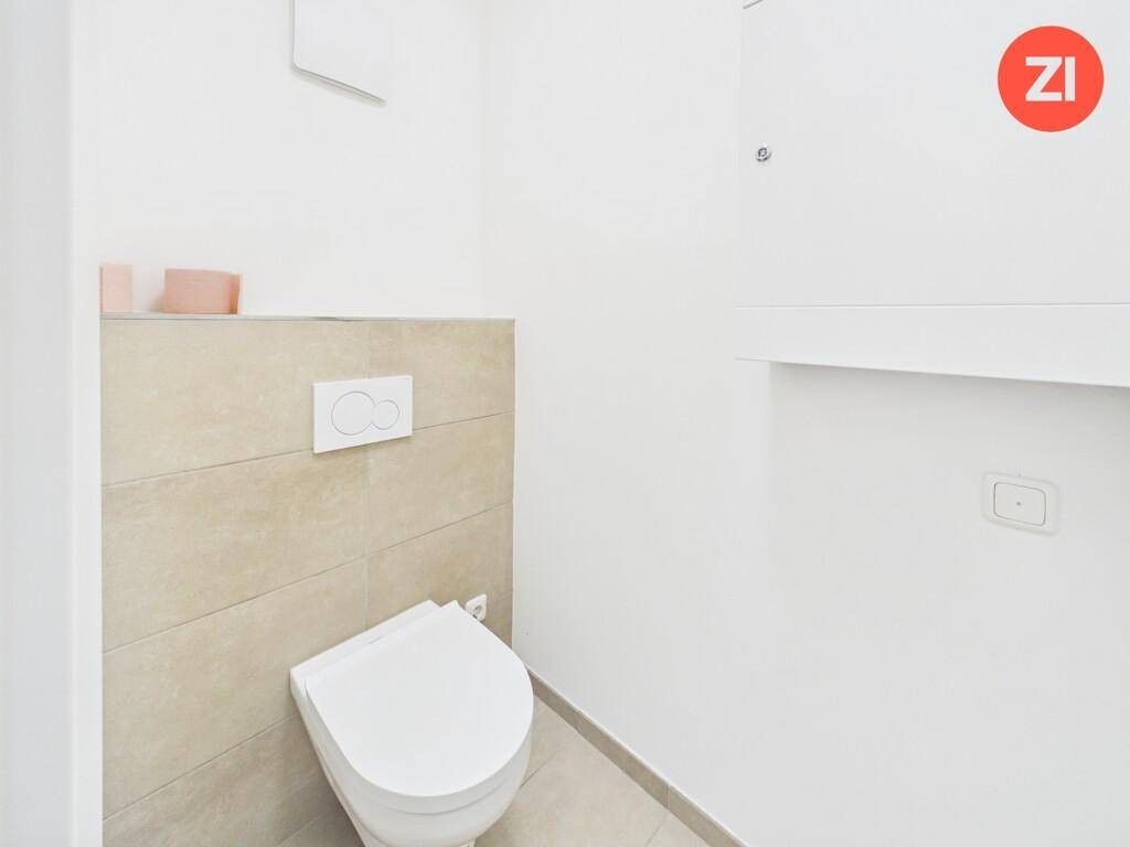 Modernes Gäste-WC mit wandhängender Toilette und beigefarbenen Fliesen an der Wand.