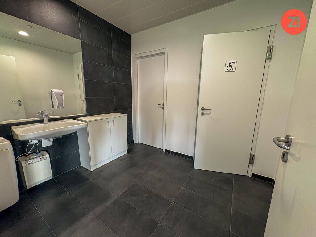 Geräumiges Badezimmer mit Waschbecken, Spiegel und einer barrierefreien Toilette, gekennzeichnet mit einem Rollstuhlsymbol.
