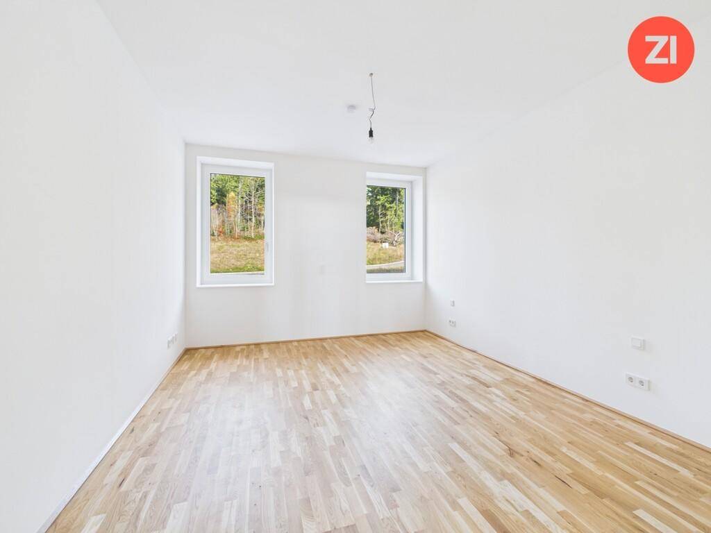 Geräumiges Schlafzimmer mit zwei Fenstern, Parkettboden und Blick auf die umliegende Natur.