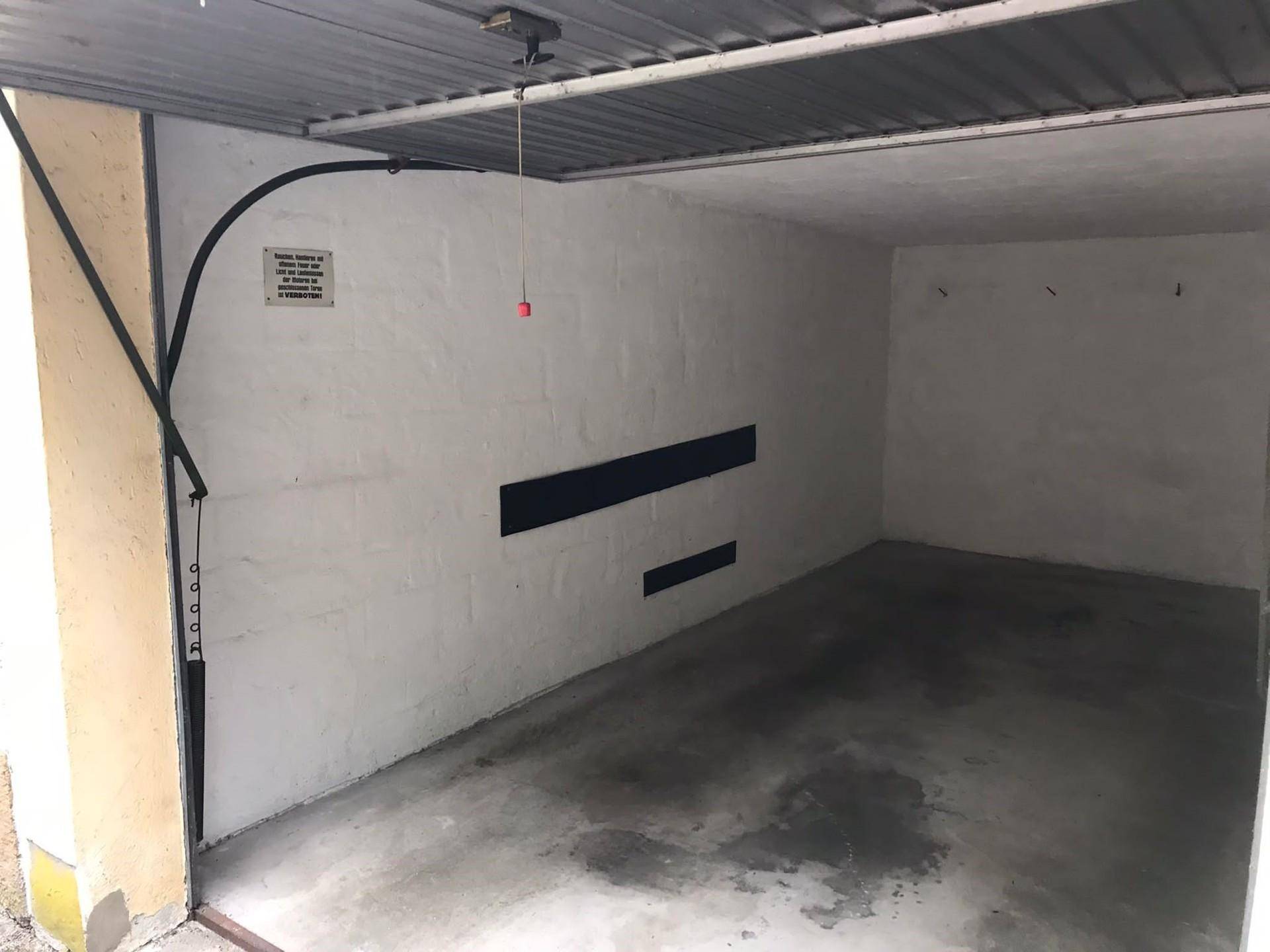 Leere Garagenbox mit weiß gestrichenen Wänden, Betonboden und Rolltor.