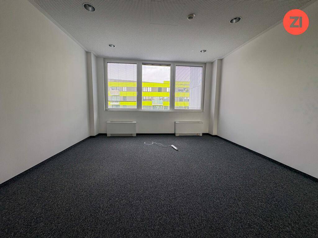 Helles Einzelbüro mit Teppichboden, großen Fenstern und Blick auf die umliegenden Gebäude.