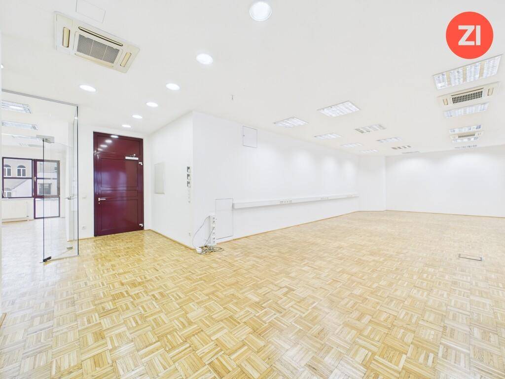 Heller Büroraum mit Parkettboden, weißen Wänden und einer markanten roten Tür, ergänzt durch moderne Glaswände.