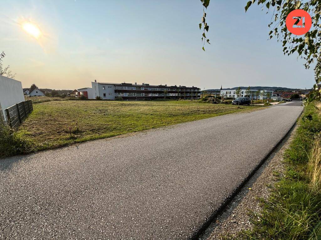 Weitläufiges, unbebautes Grundstück mit Grasfläche und angrenzender Straße unter strahlendem Himmel.