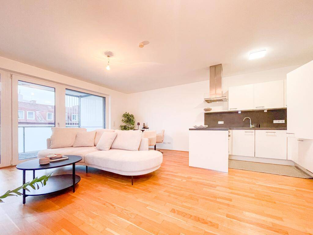 Geräumige offene Wohnküche mit hellem Sofa, Holzboden und direktem Zugang zum Balkon.