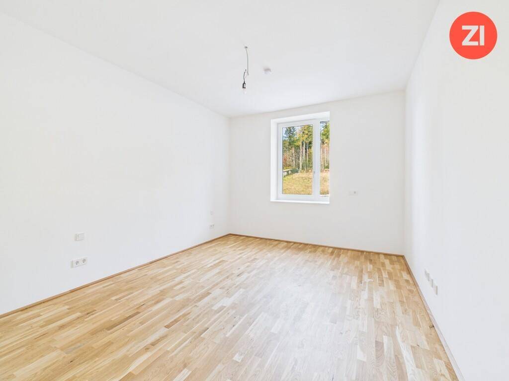 Ruhiges Schlafzimmer mit hellem Parkettboden und einem Fenster mit Ausblick ins Grüne.