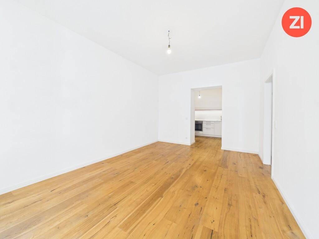 Geräumiges Wohnzimmer mit Holzboden und offenem Zugang zur modernen Küchenzeile.