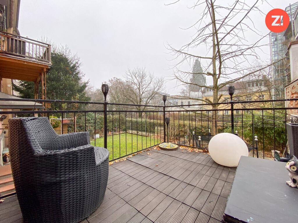 Möblierte Terrasse mit Holzboden und Blick auf den Garten und die umliegenden Gebäude.