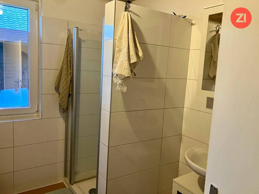 Helles Badezimmer mit Duschkabine, Waschbecken und einem Fenster für natürliche Belüftung.