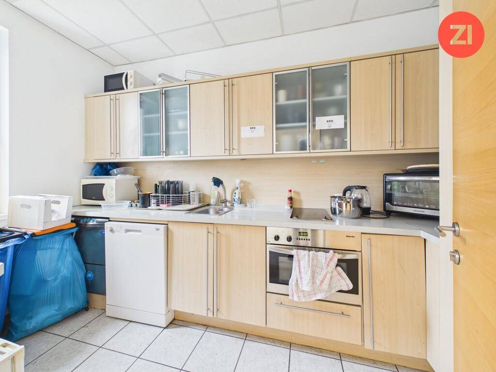 Funktionale Teeküche mit hellen Holzschränken, Spülmaschine, Backofen und Mikrowelle.