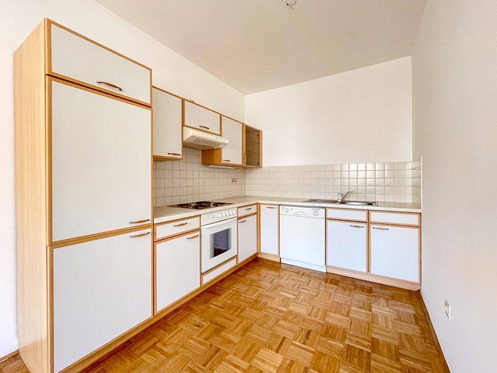 Funktionale Einbauküche mit weißen Fronten, Holzdetails und Parkettboden.