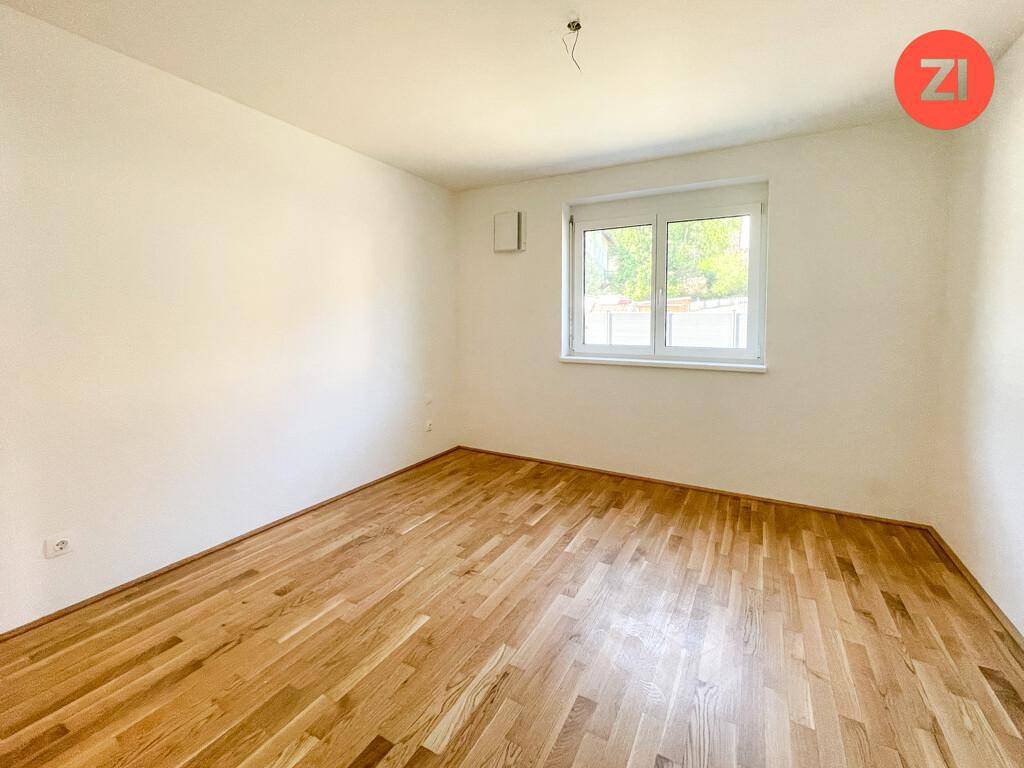 Leeres, helles Zimmer mit Parkettboden und einem großen Fenster, ideal als Schlafzimmer.