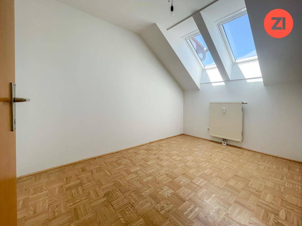 Gemütliches Zimmer im Dachgeschoss mit Parkettboden, Dachschrägen und zwei großen Dachfenstern.