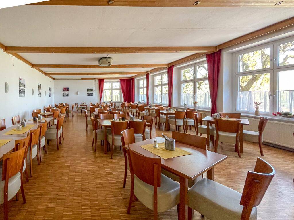 Großer Speisesaal mit vielen Holztischen und Stühlen, Holzboden und sichtbaren Deckenbalken.