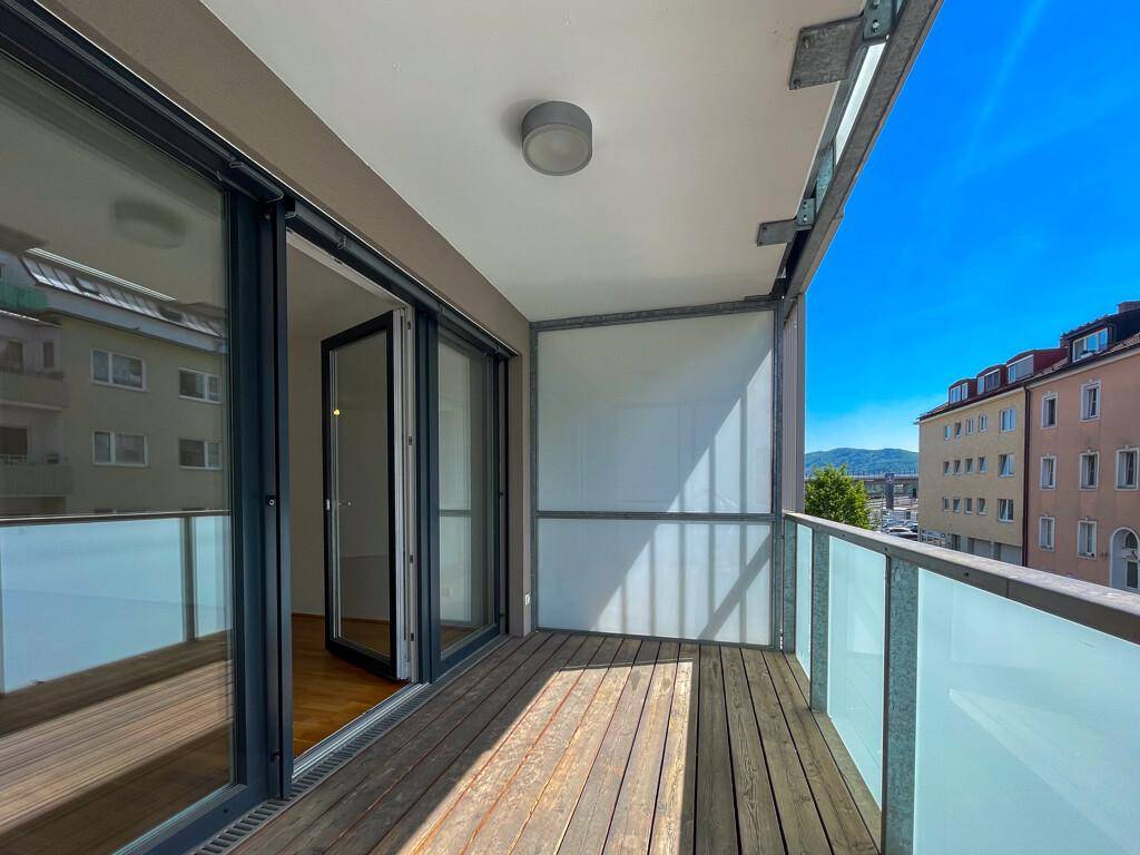 Moderner Balkon mit Holzboden, Glasgeländer und weitem Blick über die Stadt.